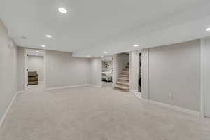 Finished below grade area with recessed lighting, stacked washer / dryer, light colored carpet, and stairs