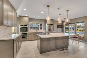 Kitchen with hanging light fixtures, stainless steel appliances, light stone countertops, tasteful backsplash, and recessed lighting