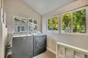 Washroom featuring vaulted ceiling, light wood-style flooring, washer and clothes dryer, and a textured wall