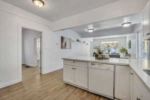 Kitchen featuring white dishwasher, white cabinets, light wood-style flooring, light stone counters, and a peninsula