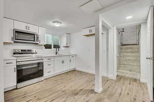 Kitchen featuring stainless steel appliances, white cabinets, light countertops, and light wood-type flooring
