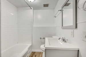 Bathroom with vanity, light wood-style flooring, bathing tub / shower combination, and a textured ceiling