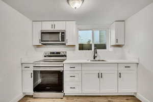 Kitchen featuring stainless steel appliances, white cabinets, light wood-style flooring, light stone countertops, and a textured ceiling