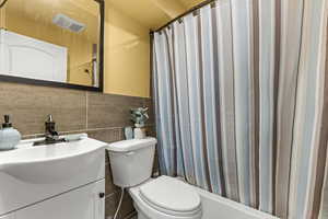 Full bath with vanity, tile walls, and shower / bath combo with shower curtain