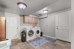 Washroom with a textured ceiling, cabinet space, washer and dryer, and light tile patterned floors