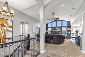 Living room with arched walkways, a stone fireplace, light colored carpet, vaulted ceiling, and light tile patterned floors