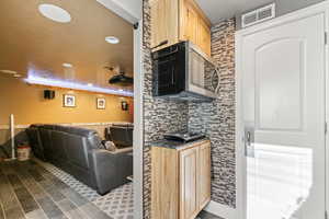Kitchen featuring light brown cabinets, open floor plan, stainless steel microwave, wood finish floors, and decorative backsplash