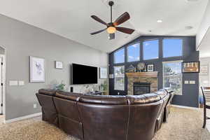 Living room featuring ceiling fan, high vaulted ceiling, plenty of natural light, a fireplace, and light carpet