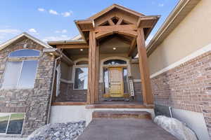 View of exterior entry with stucco siding, covered porch, and stone siding