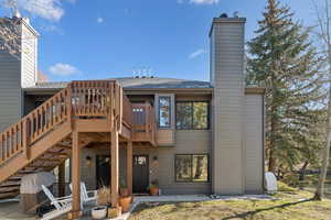 Rear view of house featuring a patio, a deck, a chimney, a shingled roof, and stairs