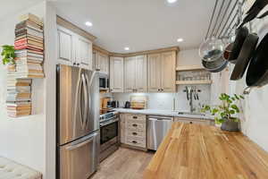 Kitchen featuring butcher block counters, appliances with stainless steel finishes, tasteful backsplash, open shelves, and light wood-type flooring