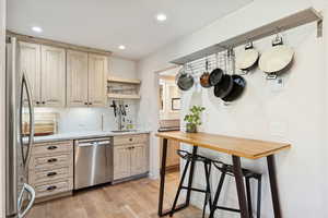 Kitchen featuring open shelves, appliances with stainless steel finishes, tasteful backsplash, light wood-type flooring, and light stone countertops