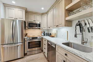 Kitchen with stainless steel appliances, light stone counters, backsplash, open shelves, and light wood-style flooring