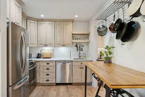 Kitchen with stainless steel appliances, open shelves, light stone countertops, decorative backsplash, and light wood-style floors