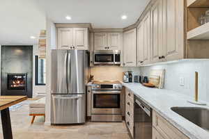 Kitchen with stainless steel appliances, light stone countertops, a large fireplace, open shelves, and recessed lighting