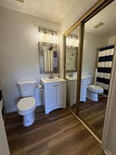 Full bath with curtained shower, a textured ceiling, two vanities, and dark wood-style flooring