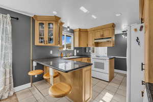 Kitchen featuring a peninsula, light tile patterned flooring, a kitchen breakfast bar, white appliances, and glass insert cabinets