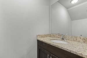 Bathroom featuring vanity, vaulted ceiling, and a textured wall