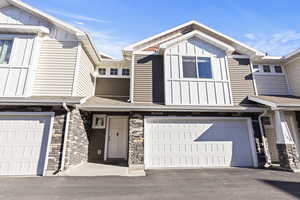 Craftsman-style house with board and batten siding, stone siding, a shingled roof, a garage, and asphalt driveway