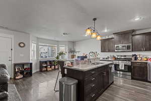 Kitchen with stainless steel appliances, a kitchen breakfast bar, dark brown cabinets, light stone countertops, and pendant lighting