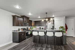 Kitchen featuring dark brown cabinetry, stainless steel appliances, a kitchen breakfast bar, a textured ceiling, and light stone counters