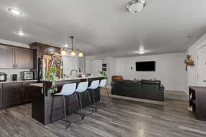 Kitchen with a breakfast bar area, light stone countertops, pendant lighting, dark brown cabinets, and freestanding refrigerator