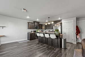 Kitchen featuring dark brown cabinetry, a kitchen bar, an island with sink, dark wood-style flooring, and hanging light fixtures