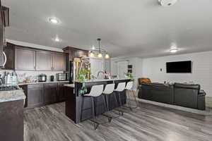 Kitchen featuring a kitchen breakfast bar, pendant lighting, light stone countertops, dark wood-style floors, and a center island with sink