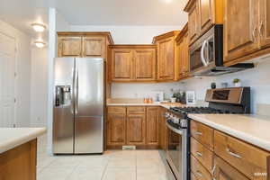 Kitchen featuring stainless steel appliances, brown cabinetry, light countertops, and light tile patterned floors