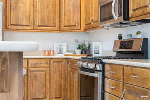 Kitchen featuring stainless steel appliances, brown cabinetry, and light countertops