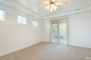 Empty room featuring a tray ceiling, carpet floors, and a ceiling fan