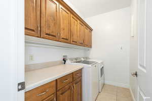 Washroom with light tile patterned flooring, cabinet space, and separate washer and dryer