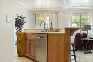 Kitchen with brown cabinets, light countertops, a kitchen island with sink, dishwasher, and hanging light fixtures