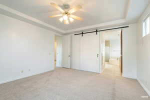 Unfurnished bedroom featuring a barn door, a raised ceiling, light carpet, and ensuite bathroom
