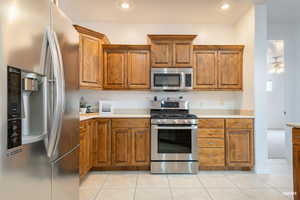 Kitchen featuring appliances with stainless steel finishes, brown cabinetry, light countertops, light tile patterned floors, and recessed lighting