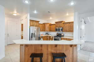 Kitchen featuring light tile patterned flooring, appliances with stainless steel finishes, a kitchen breakfast bar, brown cabinets, and light countertops