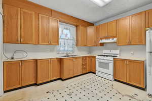 Kitchen with white appliances, light countertops, a textured ceiling, light floors, and under cabinet range hood