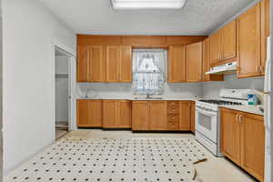 Kitchen with light countertops, white gas range, under cabinet range hood, a textured ceiling, and light floors