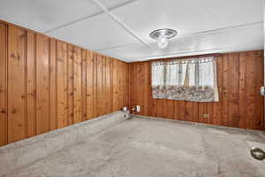 Carpeted empty room featuring wooden walls