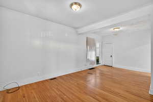 Empty room featuring hardwood / wood-style floors and beam ceiling