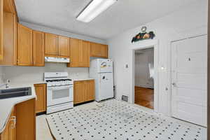 Kitchen with light countertops, white appliances, light flooring, under cabinet range hood, and a textured ceiling