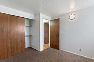 Unfurnished bedroom featuring carpet floors, a textured ceiling, and a closet