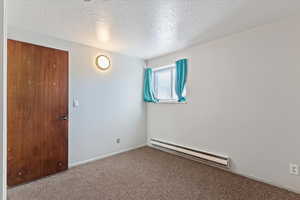 Spare room with baseboard heating, carpet floors, and a textured ceiling