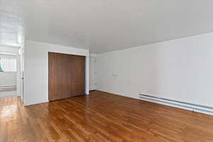 Unfurnished bedroom with wood finished floors, a baseboard heating unit, a closet, and a textured ceiling