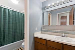 Bathroom with wallpapered walls, vanity, and shower / tub combo with curtain