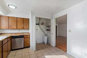 Kitchen with dishwasher, brown cabinets, light tile patterned flooring, a textured ceiling, and light countertops