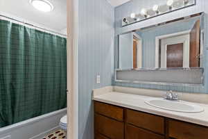 Full bath with wallpapered walls, shower / bath combo, and vanity