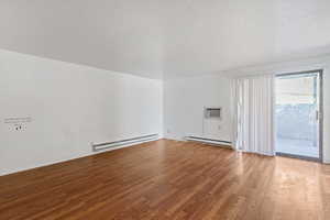 Unfurnished room featuring light wood-type flooring, a textured ceiling, a baseboard radiator, and a wall mounted AC