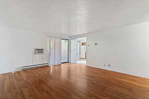 Empty room featuring a textured ceiling, wood finished floors, a baseboard heating unit, and a wall mounted air conditioner