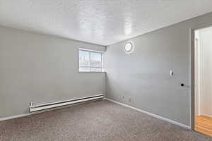 Unfurnished room with baseboard heating, carpet floors, and a textured ceiling